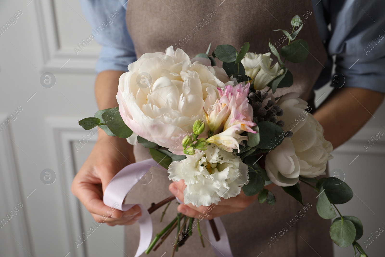 Photo of Florist creating beautiful bouquet at white wall, closeup