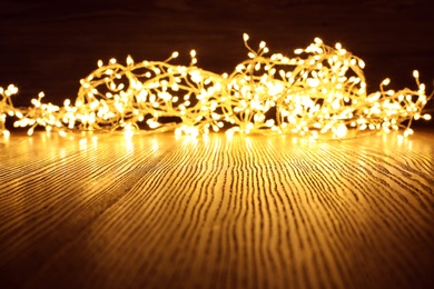 Photo of Beautiful glowing Christmas lights on wooden table. Space for text