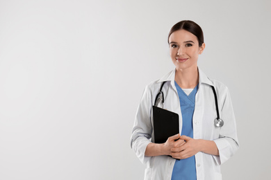 Photo of Doctor with stethoscope and clipboard on light grey background. Space for text