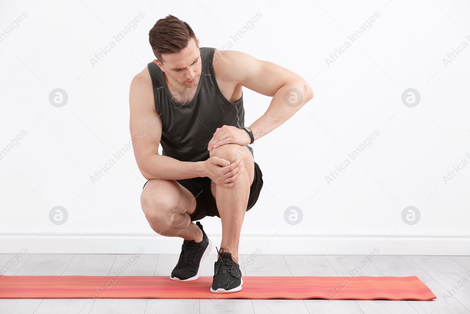 Photo of Male athlete suffering from knee pain during training indoors