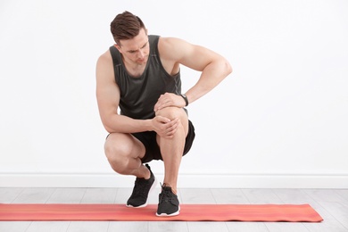 Photo of Male athlete suffering from knee pain during training indoors