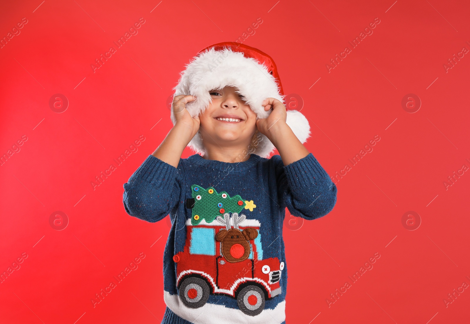 Photo of Happy little child in Santa hat on red background. Christmas celebration