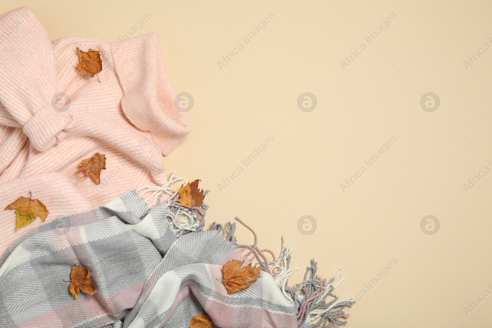 Photo of Sweater, scarf and dry leaves on beige background, flat lay with space for text. Autumn season