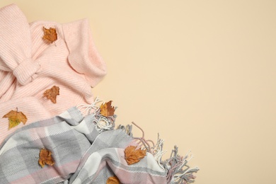 Photo of Sweater, scarf and dry leaves on beige background, flat lay with space for text. Autumn season