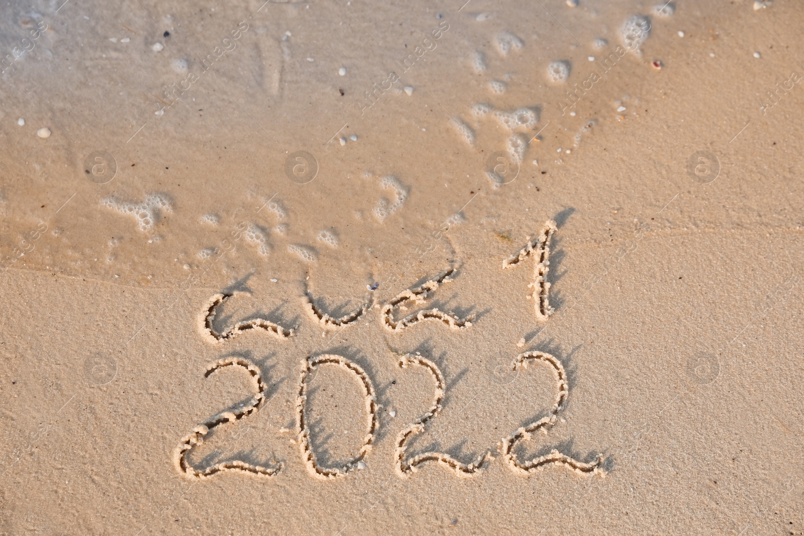 Photo of Sea wave rolling onto sandy beach with written 2021 and 2022. New Year