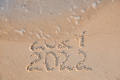 Sea wave rolling onto sandy beach with written 2021 and 2022. New Year