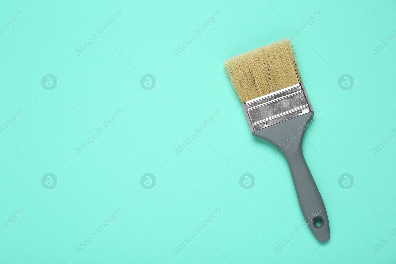 Photo of One paint brush with grey handle on turquoise background, top view. Space for text