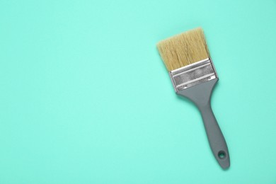 Photo of One paint brush with grey handle on turquoise background, top view. Space for text