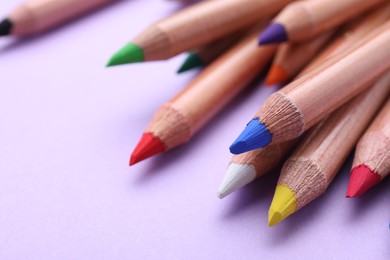 Many colorful pastel pencils on violet background, closeup. Drawing supplies