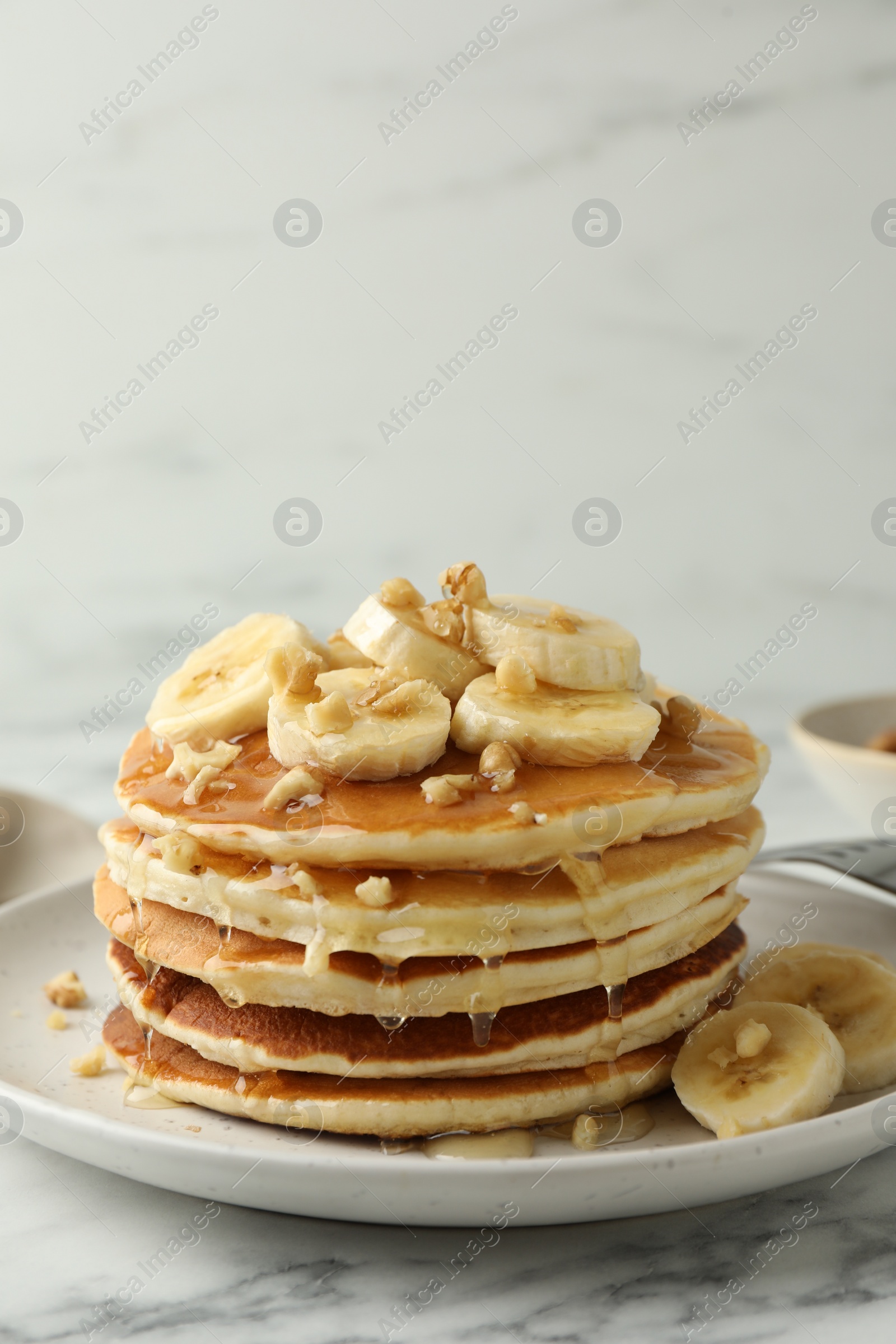 Photo of Delicious pancakes with bananas, walnuts and honey on white marble table. Space for text