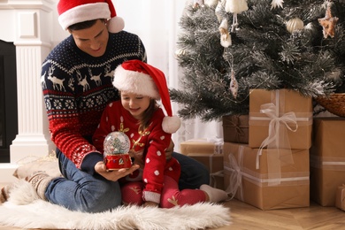 Father and daughter playing with snow globe near Christmas tree