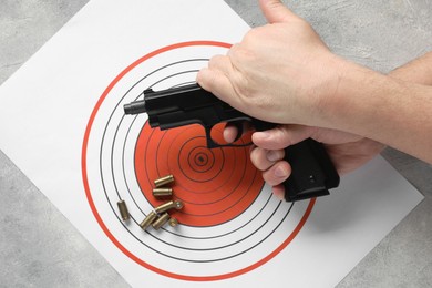 Photo of Man with handgun, shooting target and bullets at gray table, top view