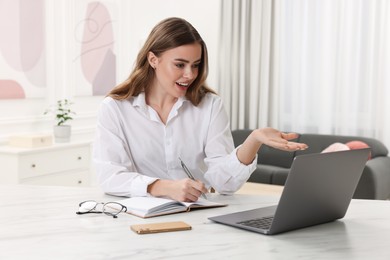 Photo of Happy woman having video chat via laptop at white table in room