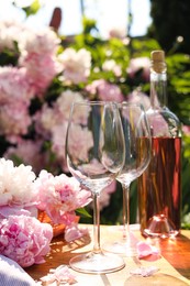 Photo of Bottle of rose wine and glasses with beautiful peonies on wooden table in garden