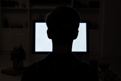 Photo of Teenage boy using computer at night, back view. Internet addiction