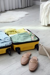 Open suitcase packed for trip, handbag and shoes on floor indoors