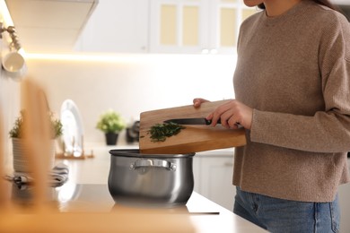 Photo of Woman adding cut parsley into pot with soup in kitchen, closeup