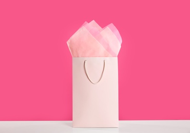 Photo of Gift bag with paper on white table against pink background