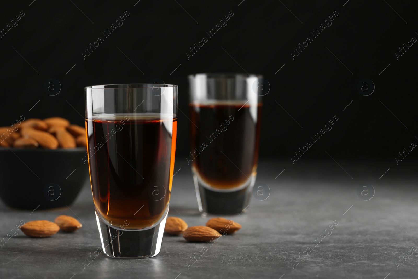 Photo of Glasses with tasty amaretto liqueur and almonds on gray table, closeup. Space for text