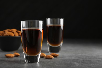Photo of Glasses with tasty amaretto liqueur and almonds on gray table, closeup. Space for text
