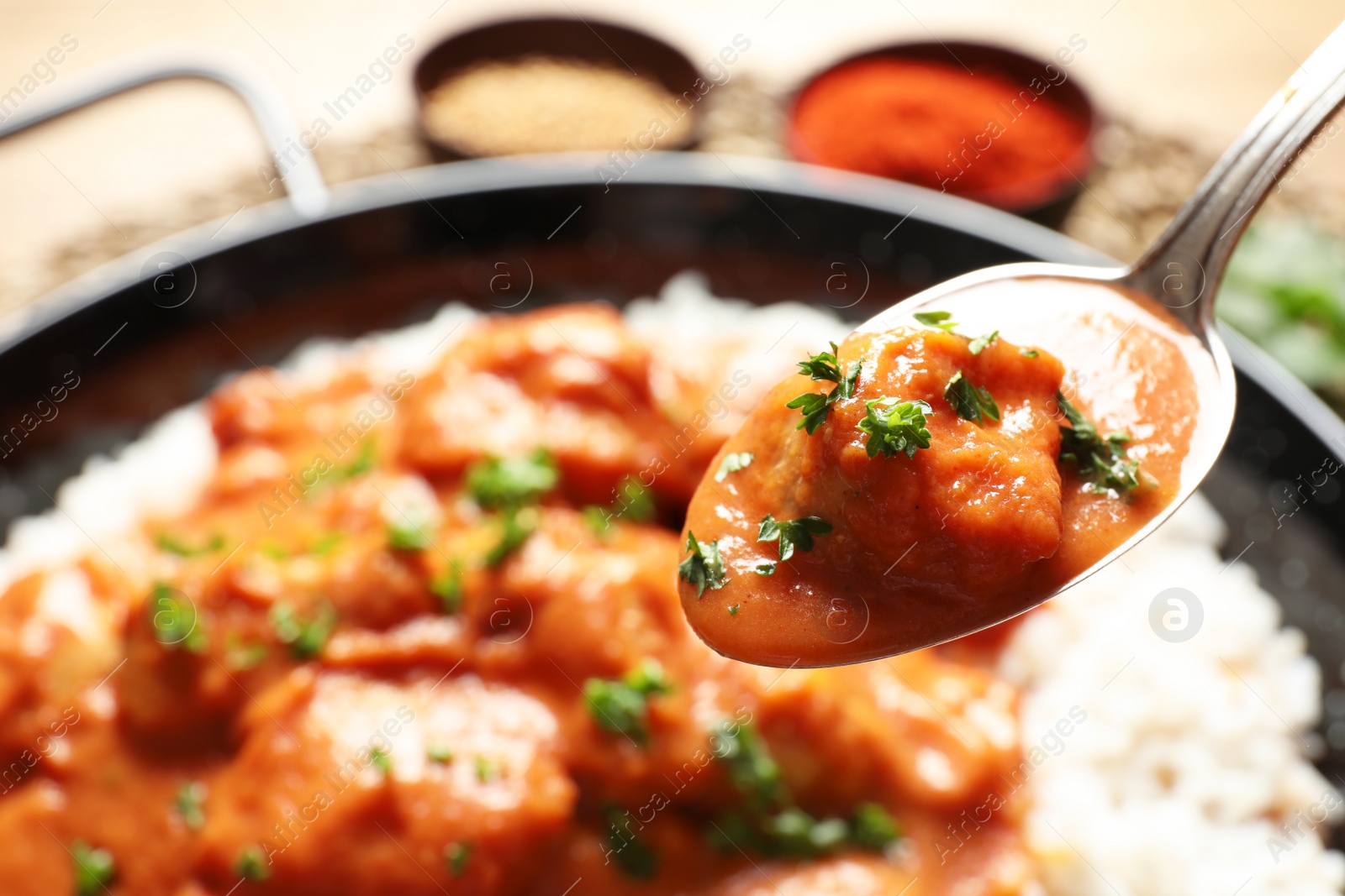 Photo of Tasty butter chicken in spoon over dish with meal, closeup