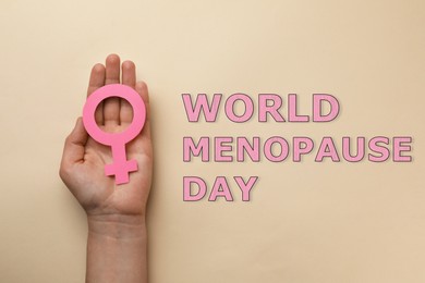 World Menopause Day. Woman holding female gender sign on beige background, top view