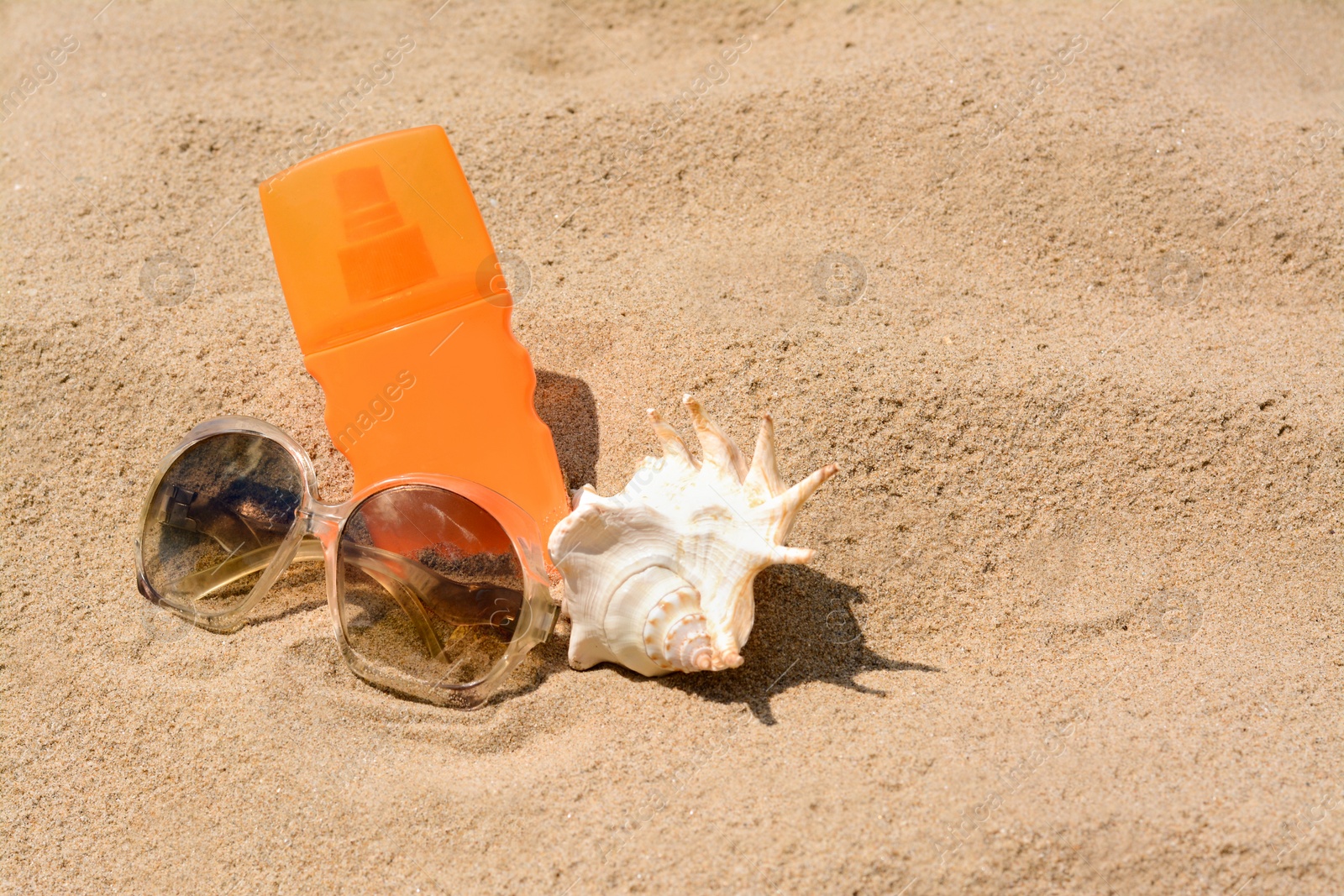 Photo of Bottle with sun protection spray, sunglasses and seashell on sandy beach, space for text