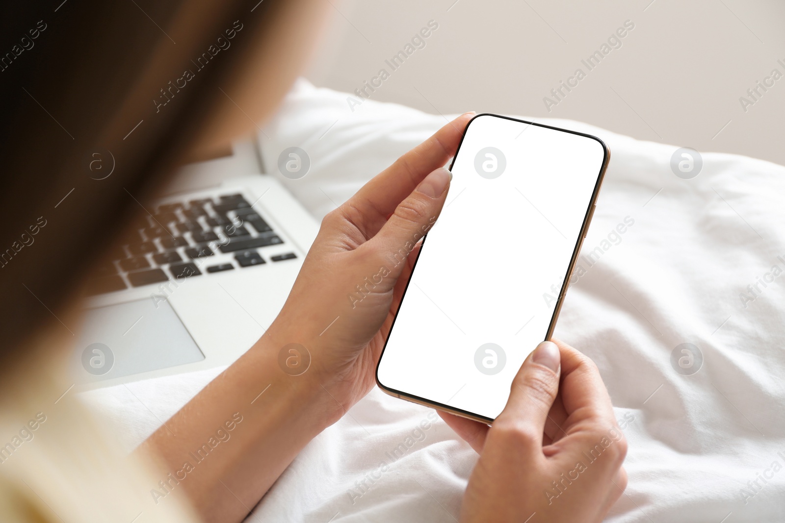 Image of Young woman holding mobile phone with empty screen in hands on bed at home, closeup