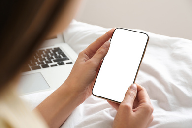 Young woman holding mobile phone with empty screen in hands on bed at home, closeup