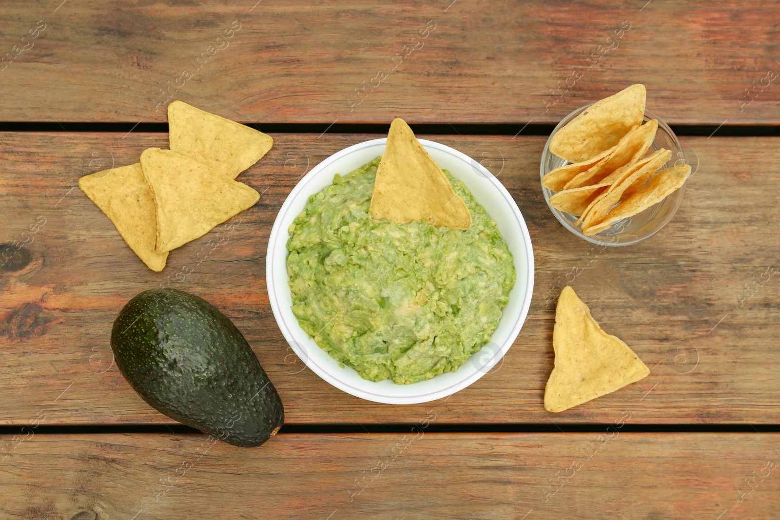 Photo of Delicious guacamole, avocado and nachos on wooden table, flat lay