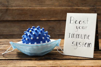 Photo of Notebook with phrase Boost your Immune System and medical mask on wooden table