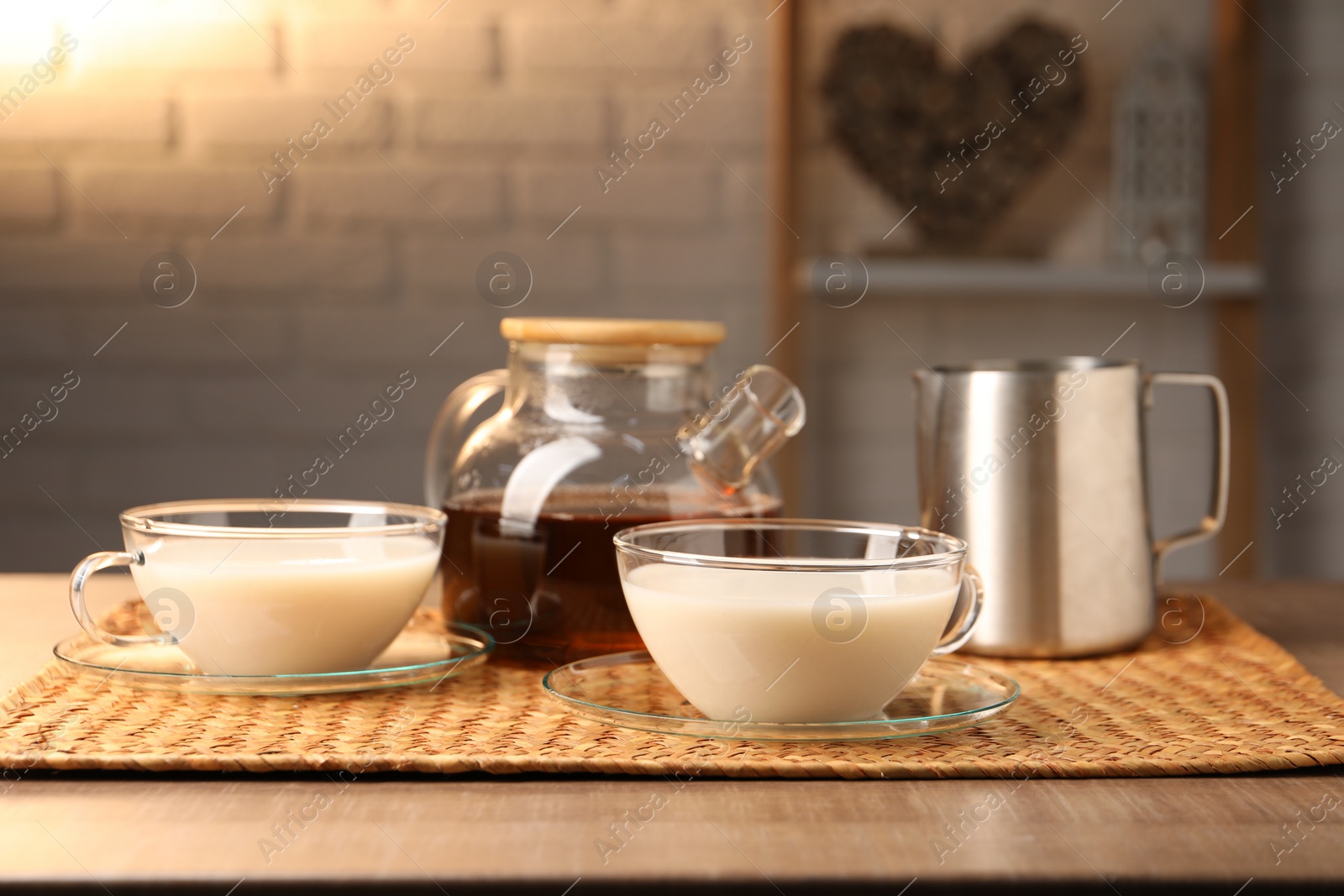 Photo of Tasty milk in glass cups, pitcher and teapot with tea on wooden table