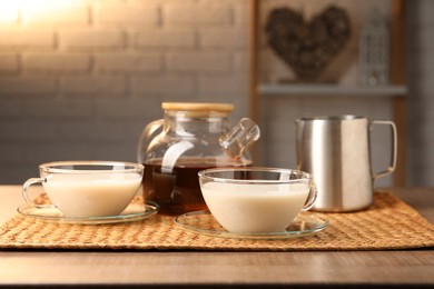 Photo of Tasty milk in glass cups, pitcher and teapot with tea on wooden table