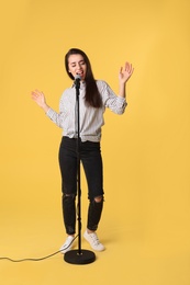 Photo of Young woman wearing casual clothes singing in microphone on color background