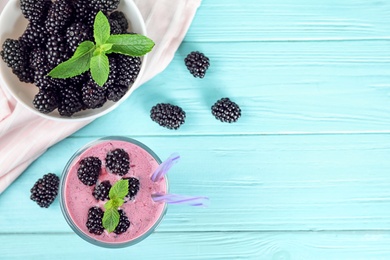 Flat lay composition with glass of delicious blackberry smoothie on light blue wooden background. Space for text