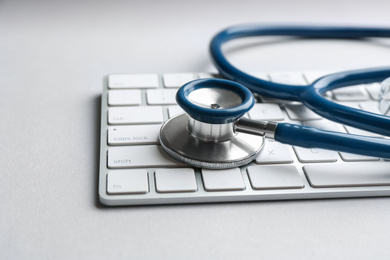Photo of Keyboard and stethoscope on light grey table, closeup. Concept of technical support