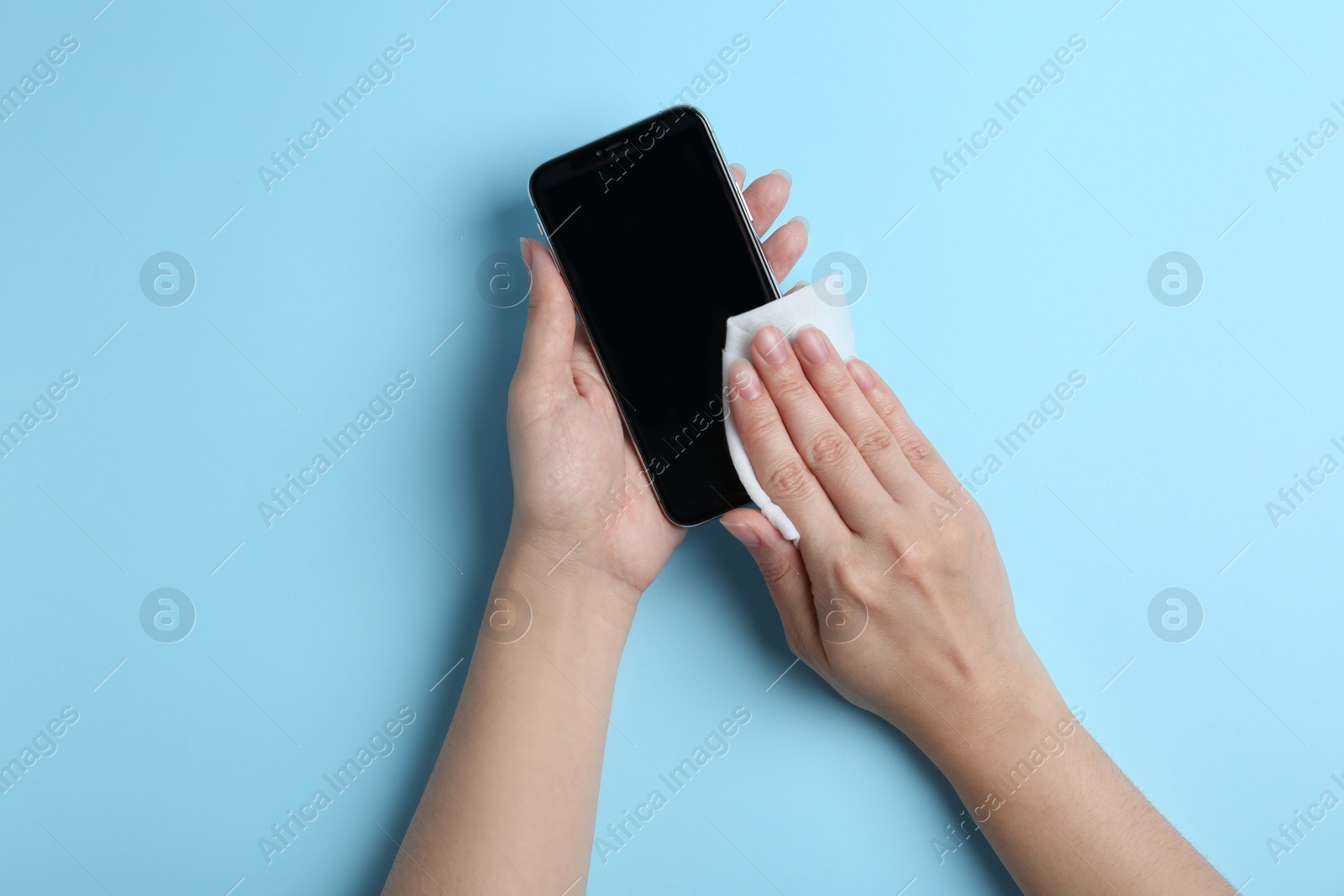 Photo of Woman cleaning mobile phone with antiseptic wipe on light blue background, top view