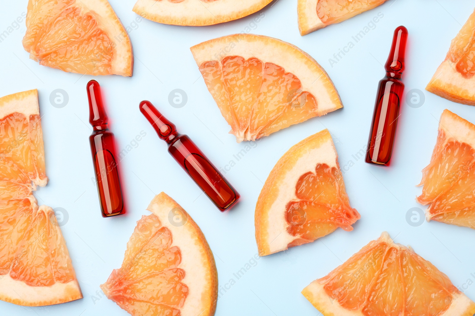 Photo of Skincare ampoules with vitamin C and slices of grapefruit on light blue background, flat lay