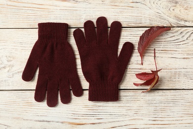 Photo of Stylish woolen gloves and dry leaves on white wooden table, flat lay