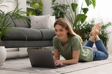 Photo of Woman using laptop surrounded by beautiful potted houseplants at home