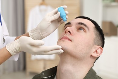 Photo of Doctor applying medical drops into young man's eye indoors