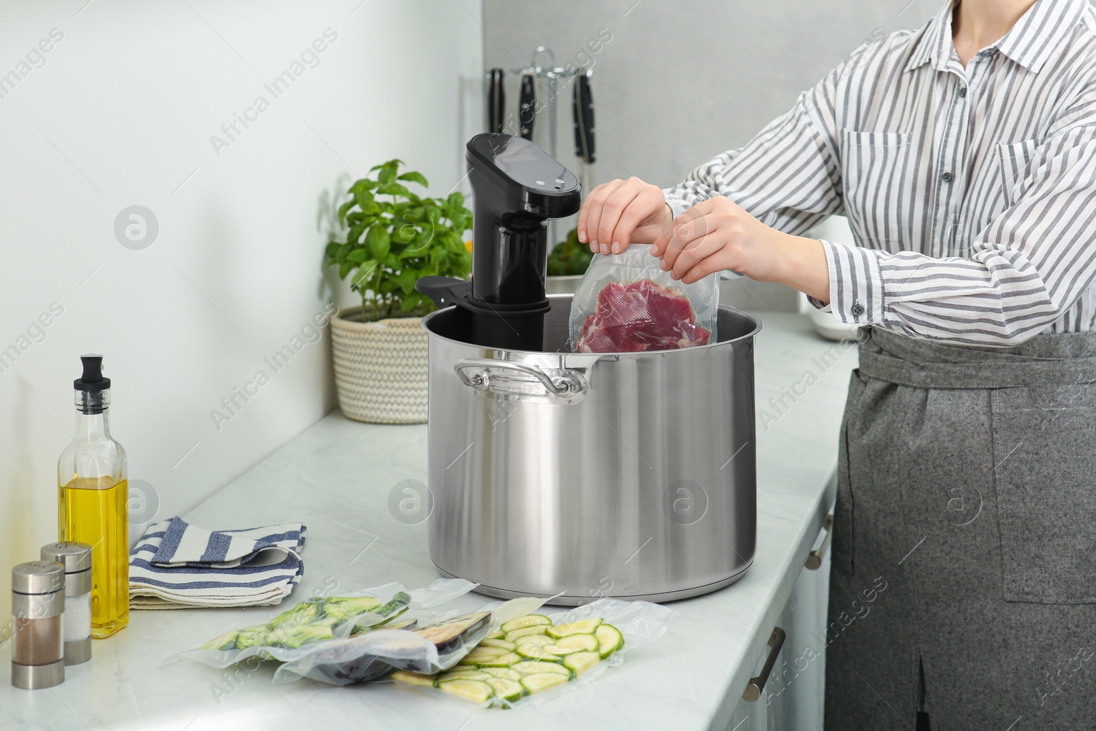 Photo of Woman putting vacuum packed meat into pot in kitchen, closeup. Thermal immersion circulator for sous vide cooking