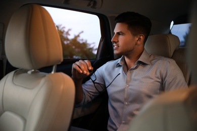 Handsome man with glasses on backseat of modern car