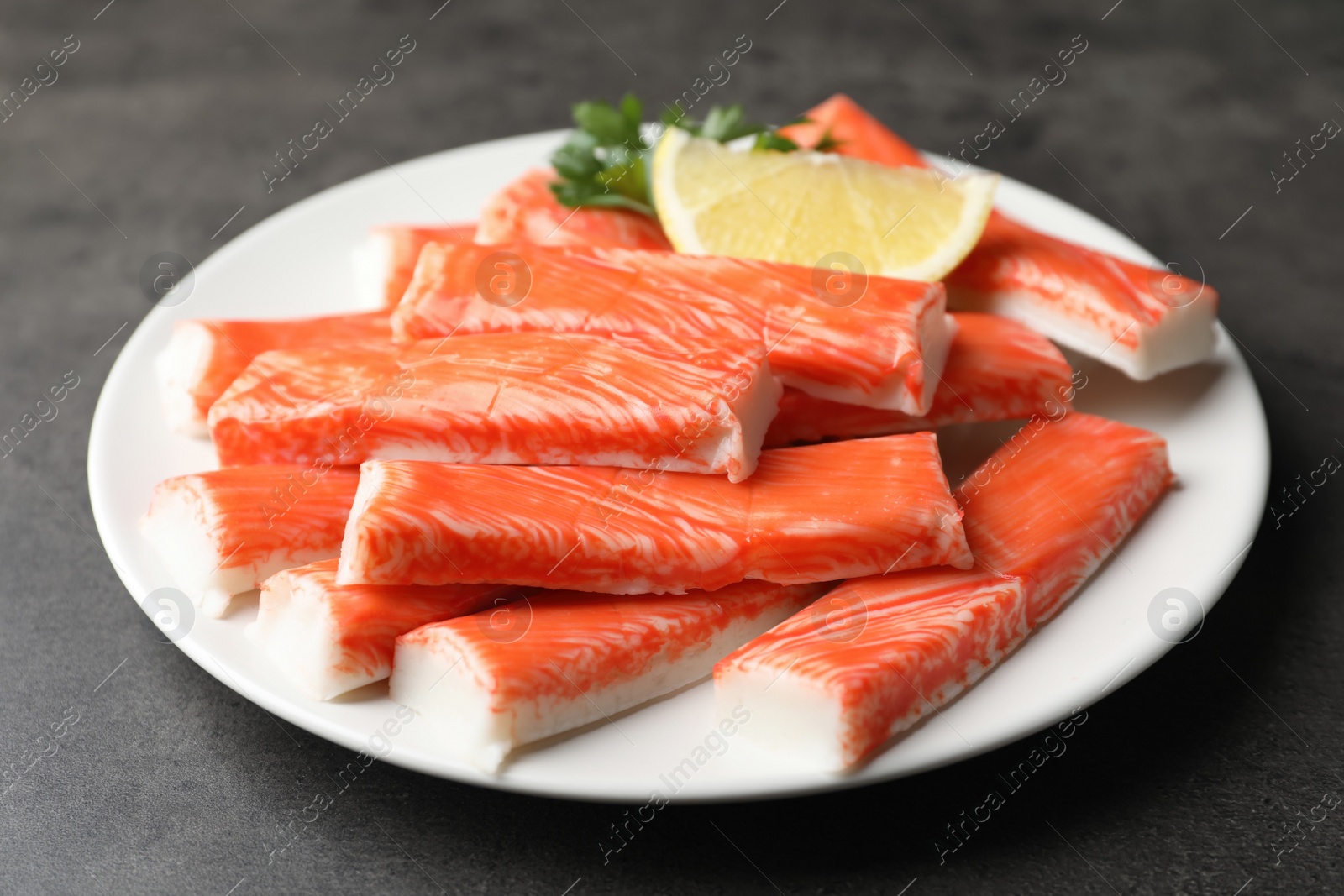 Photo of Plate of fresh crab sticks with lemon on grey table, closeup