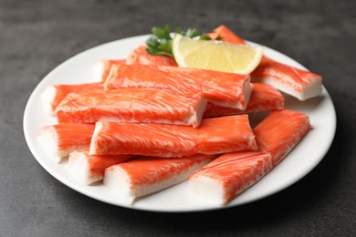 Plate of fresh crab sticks with lemon on grey table, closeup