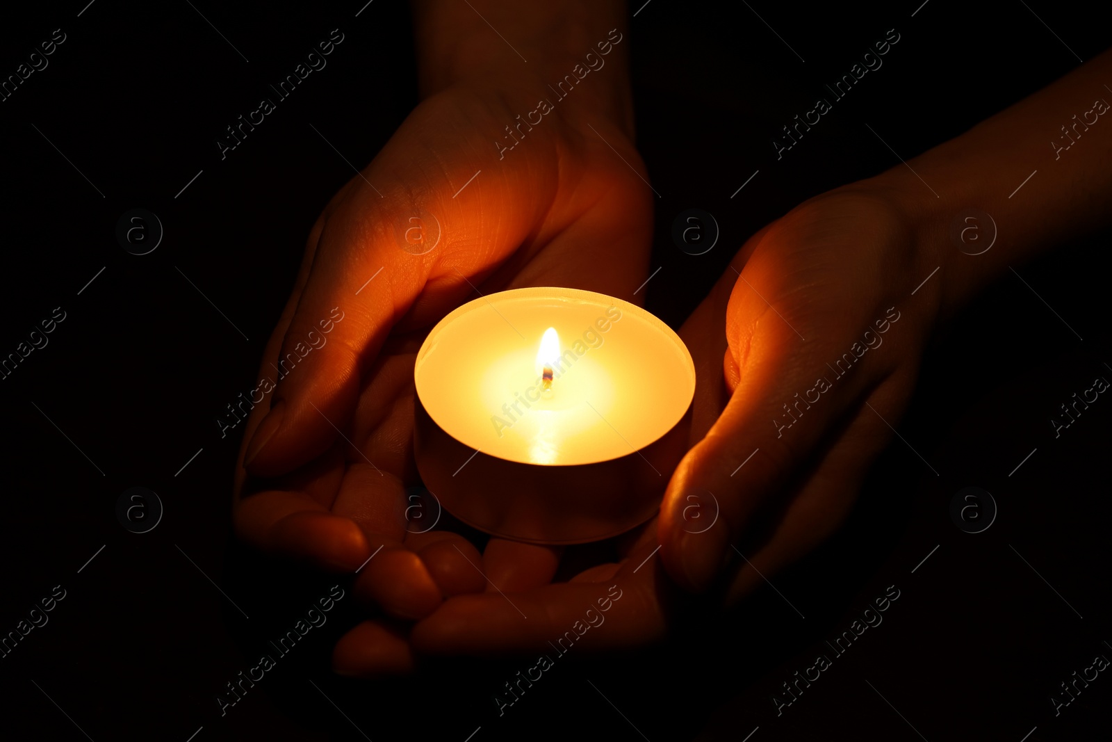 Photo of Woman holding burning candle in hands on black background, closeup