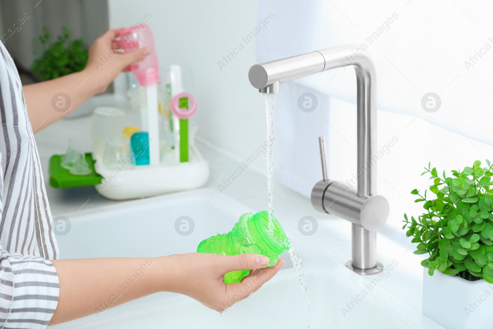 Photo of Woman washing baby bottle under stream of water in kitchen, closeup