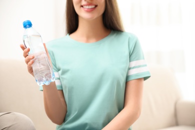 Photo of Woman with bottle of fresh water indoors, closeup