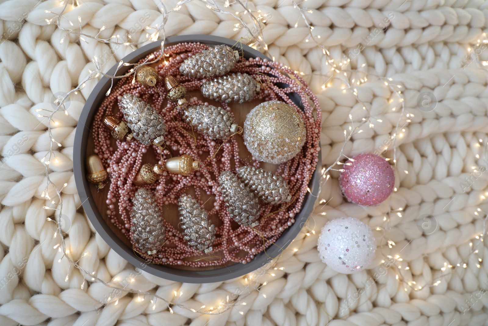 Photo of Beautiful Christmas tree baubles and fairy lights on white knitted fabric, above view