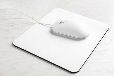 Photo of Modern wired optical mouse and pad on white wooden table